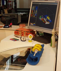 Na obrázku je barevná 3D tiskárna Contex Designmate a její výstupy